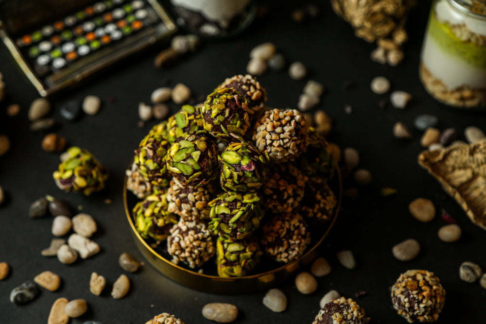 Stack of green and brown cannabis buds on a dark surface with stones and a small container.