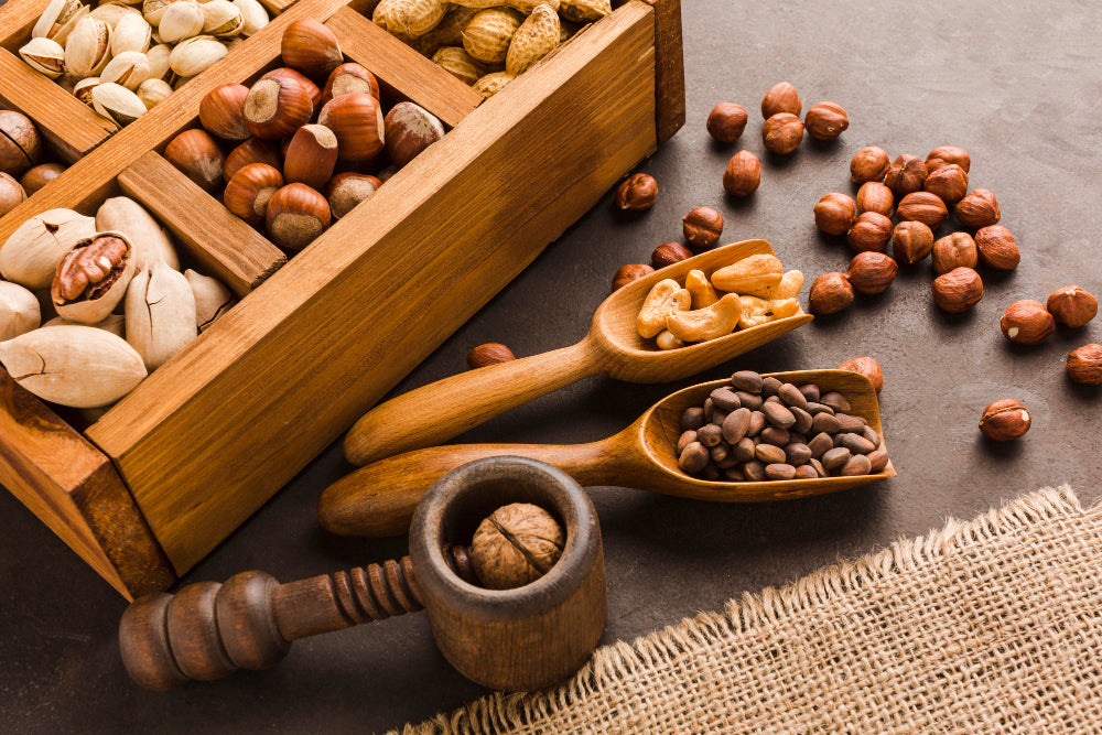 Assorted nuts in a wooden box with wooden spoons on a dark surface.