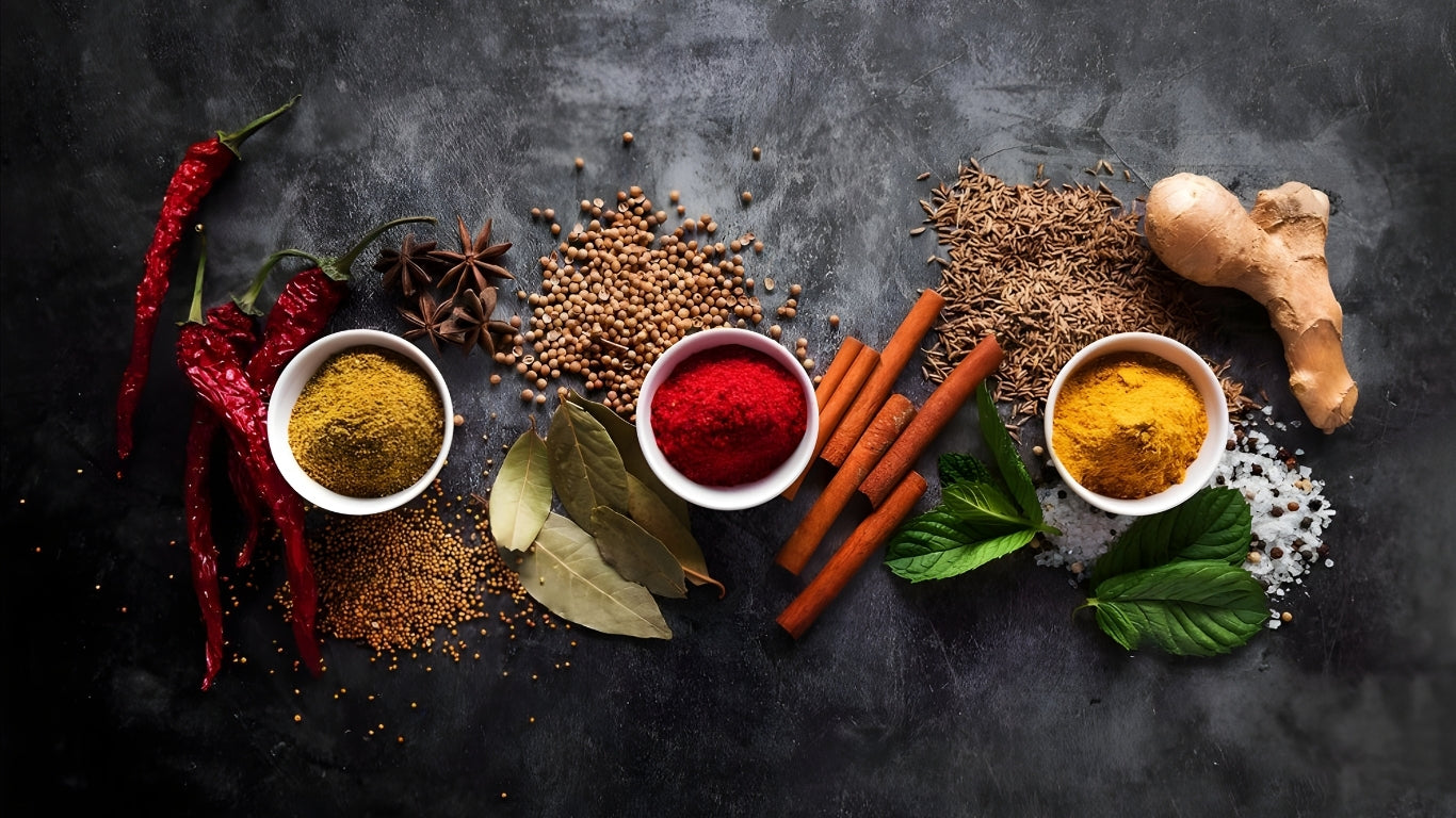 Spices and herbs on a dark surface with bowls of different colored powders.